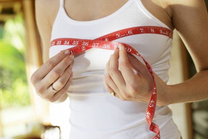 A woman measuring chest with a red tape measure against a blurred background